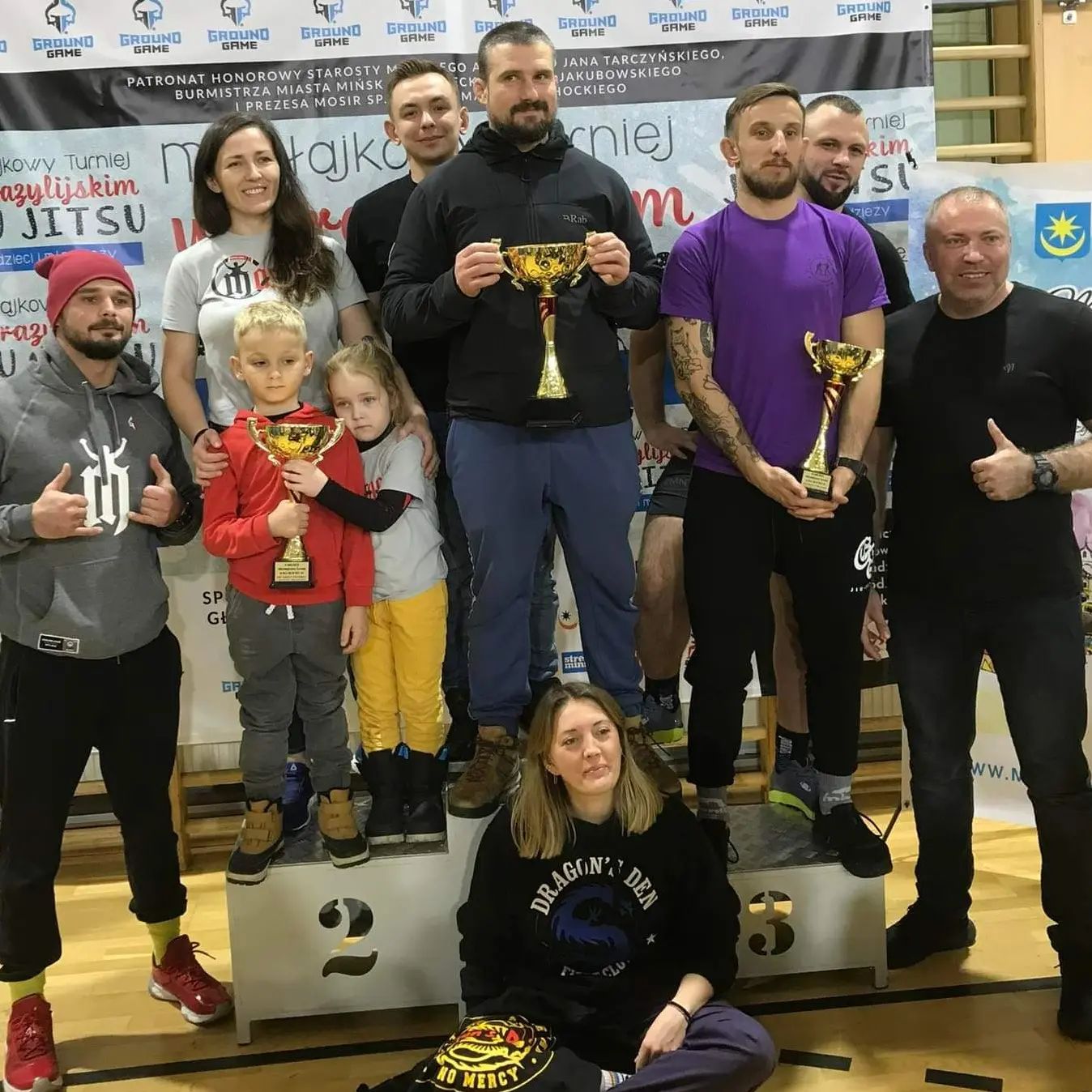 BJJ team seating at the platform holding medals and trophies